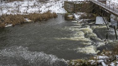 Bir yaya köprüsünün altındaki kış nehrinde kaynar su. Soyut arkaplan. Mesaj için yer var. Doğa kavramları.