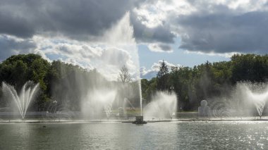 Çeşmeden su. Bulutlu gökyüzünün arkasındaki çeşme akıntısının tepesinde. Nehirdeki çeşme dramatik gökyüzüne karşı. Şehir manzarası görünümü.