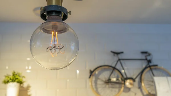 有效的白炽灯灯泡会把电浪费在用小自行车和花盆装饰的墙壁上 装饰古董爱迪生灯泡 案文的篇幅 — 图库照片