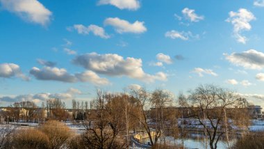 Bulutlu parlak mavi gökyüzüne karşı genç bir şehir parkı. Şehir manzarası. Şehrin ilk karı. Metin için boşluk.
