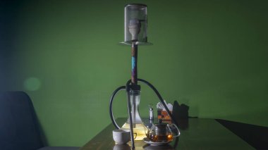 Geleneksel Arap shisha 'sı ve mercekli çay. Koyu yeşil arka planda bir çaydanlık çay ve nargile. Havalı nargile ve çaydanlık. Salon kavramları. Metin için boşluk.