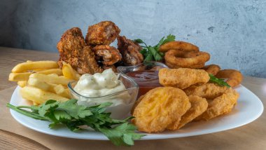 Atıştırmalık tabaklar - peynir çubukları, tavuk nugget, soğan halkaları, patates kızartması ve soslar. Bira tahtası. Yatay fotoğraf. Bar menüsü için fotoğraf.