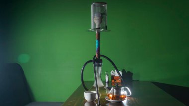 Geleneksel Arap shisha 'sı ve mercekli çay. Koyu yeşil arka planda bir çaydanlık çay ve nargile. Havalı nargile ve çaydanlık. Salon kavramları. Metin için boşluk.