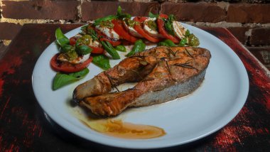 Kiraz domatesli Caprese salatası, mozzarella tostu ve kırmızı tuğla duvar arkasında ızgara somon balığı. Gıda arkaplanı.