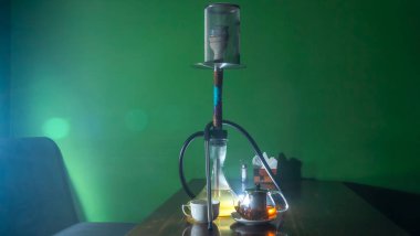 Geleneksel Arap shisha 'sı ve mercekli çay. Koyu yeşil arka planda bir çaydanlık çay ve nargile. Havalı nargile ve çaydanlık. Salon kavramları. Metin için boşluk.