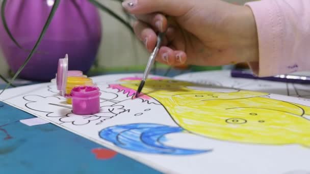 Um close-up de uma mão de crianças pintando um unicórnio com tinta rosa em uma mesa azul — Vídeo de Stock