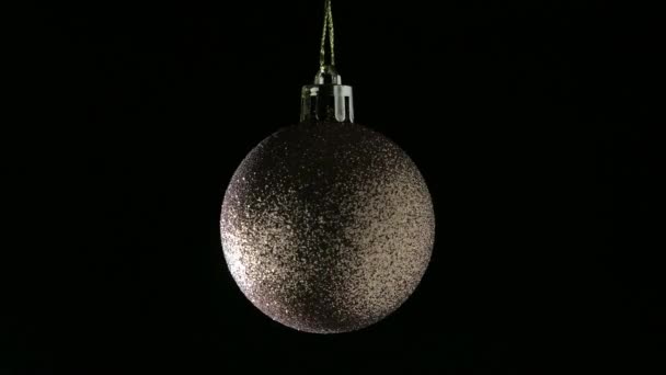 Un primer plano de una brillante bola de árbol de Navidad girando sobre un fondo negro — Vídeo de stock