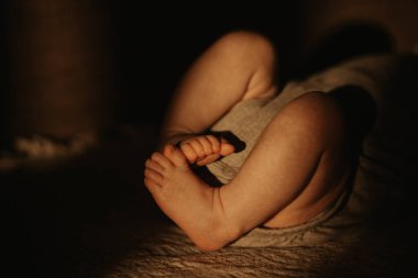 Yeni doğmuş bir bebeğin güneş ışığında kanepede yatarken giydiği kıyafetle bacak bacak bacak üstüne attığı yakın plan bir fotoğraf..