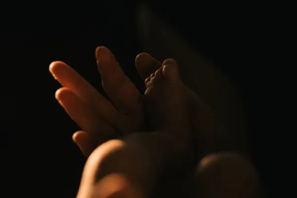 新生児のかかとを握っている母親の手のひらのクローズアップ写真 夕方の太陽の下で幼児の足 — ストック写真