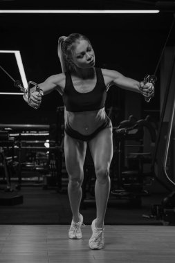 Uzun sarı saçlı fit bir kadın spor salonundaki kablolu TV makinesinde göğüs egzersizi yapıyor. Bir kız göğüs kaslarını çalıştırıyor..