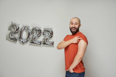 Sakallı kel bir adam 2022 yılındaki balonların yanında aşıdan sonra omzunda tıbbi bir yara bandı gösteriyor..