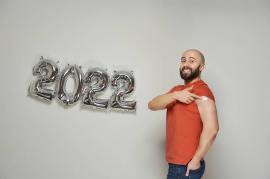 Sakallı onurlu kel bir adam, Coronavirus 'a (Covid-19) karşı aşıdan sonra omzunda tıbbi alçı gösteriyor..
