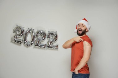 Noel Baba şapkalı mutlu ve kel bir adam, Coronavirus (Covid-19) aşısından sonra omuzunda alçı taşıyor..