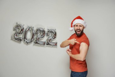 Noel Baba şapkalı kel bir adam çığlık atıyor ve Coronavirus (Covid-19) 'a karşı aşılandıktan sonra alçıyla biceps gösteriyor..