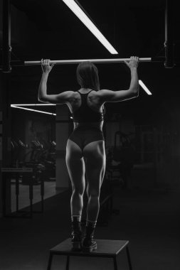 Sportif bir kadının spor salonunda barfiks çekmeye hazırlanırken çekilmiş bir fotoğrafı. Kaslı esmer bir kız siyah bluz giyer ve kısa şort giyer..