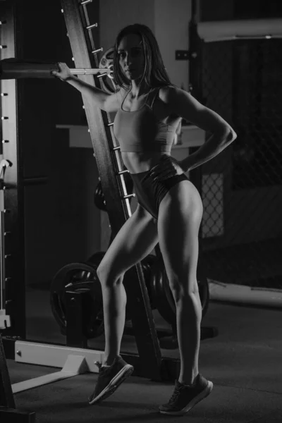 一张全长的照片 照片上的一个女运动员正手按在体操馆蹲架上的杠铃上 一个身强力壮的黑发女孩穿着珊瑚色上衣和高腰围短裤 — 图库照片