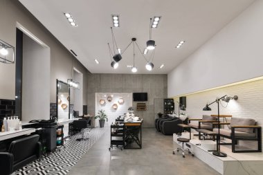 Manikür salonu ve siyah lambalar ve beton duvarlı berberden oluşan modern bir kuaför salonu. Aynalar, sandalyeler, yıkamalar ve diğer ekipmanlar kuaförde..