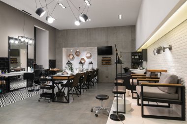 Manikür salonu ve siyah lambalar ve beton duvarlı berberden oluşan modern bir kuaför salonu. Aynalar, sandalyeler, yıkamalar ve diğer ekipmanlar kuaförde..