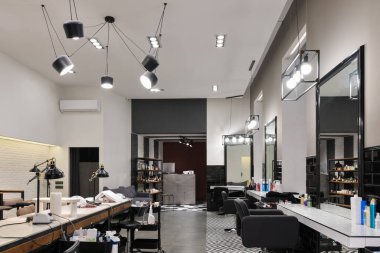Manikür salonu ve siyah lambalar ve beton duvarlı berberden oluşan modern bir kuaför salonu. Aynalar, sandalyeler, yıkamalar ve diğer ekipmanlar kuaförde..