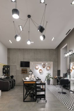 Manikür salonu ve siyah lambalar ve beton duvarlı berberden oluşan modern bir kuaför salonu. Aynalar, sandalyeler, yıkamalar ve diğer ekipmanlar kuaförde..