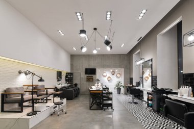 Manikür salonu ve siyah lambalar ve beton duvarlı berberden oluşan modern bir kuaför salonu. Aynalar, sandalyeler, yıkamalar ve diğer ekipmanlar kuaförde..