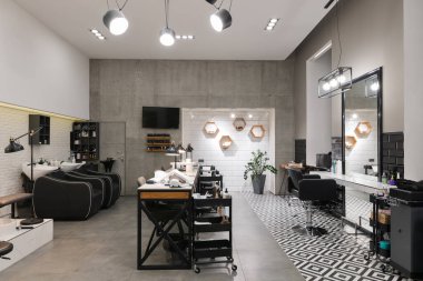 Manikür salonu ve siyah lambalar ve beton duvarlı berberden oluşan modern bir kuaför salonu. Aynalar, sandalyeler, yıkamalar ve diğer ekipmanlar kuaförde..