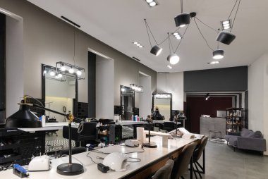 Manikür salonu ve siyah lambalar ve beton duvarlı berberden oluşan modern bir kuaför salonu. Aynalar, sandalyeler, yıkamalar ve diğer ekipmanlar kuaförde..