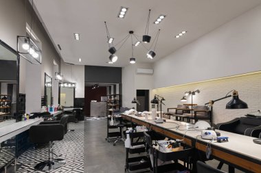 Manikür salonu ve siyah lambalar ve beton duvarlı berberden oluşan modern bir kuaför salonu. Aynalar, sandalyeler, yıkamalar ve diğer ekipmanlar kuaförde..