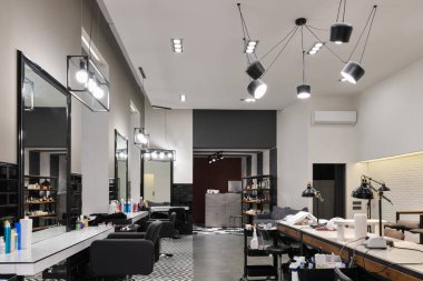 Manikür salonu ve siyah lambalar ve beton duvarlı berberden oluşan modern bir kuaför salonu. Aynalar, sandalyeler, yıkamalar ve diğer ekipmanlar kuaförde..