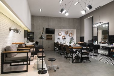 Manikür salonu ve siyah lambalar ve beton duvarlı berberden oluşan modern bir kuaför salonu. Aynalar, sandalyeler, yıkamalar ve diğer ekipmanlar kuaförde..