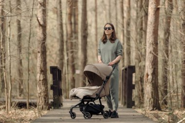 Mom is walking on a wooden walkway with a child who is sleeping in the stroller