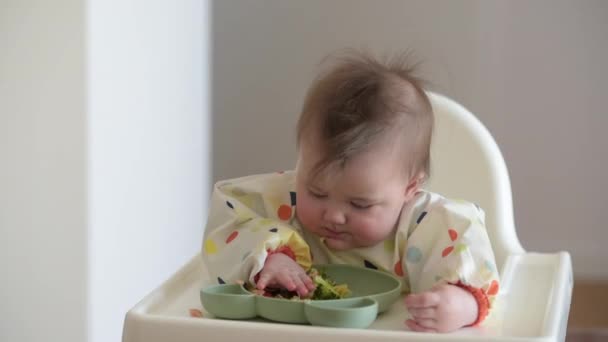 An infant 7-month caucasian girl is choosing the food with bare hands — Stockvideo