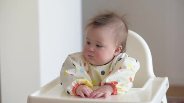 Baby meisje is het controleren van het diner terwijl zitten in een witte kinderstoel. — Stockvideo