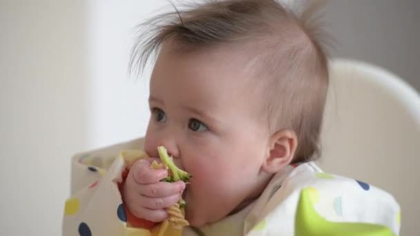 An infant 7-month caucasian girl is eating broccoli with bare hands. — Video