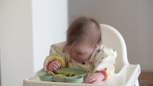 Een baby 7 maanden Kaukasisch meisje eet pasta met blote handen. — Stockvideo