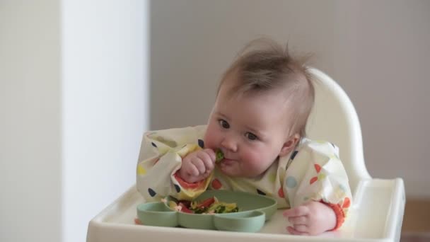 Een baby 7 maanden Kaukasisch meisje eet met blote handen — Stockvideo