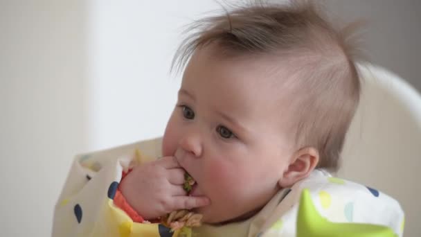Een kind van 7 maanden oud eet broccoli en tonijn met blote handen.. — Stockvideo