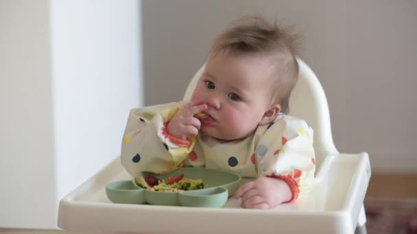 An infant 7-month caucasian girl is eating pasta with bare hands — Stockvideo