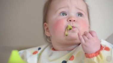 Çıplak elleriyle brokoli yiyen 7 aylık bir kızın yakın plan fotoğrafı.