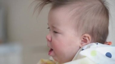 Öğle yemeği sırasında öksüren, 7 aylık beyaz bir kızın yakın plan fotoğrafı.