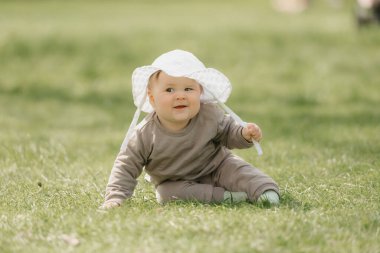 Beyaz panama şapkalı 7 aylık bir çocuk çayırda eğleniyor..