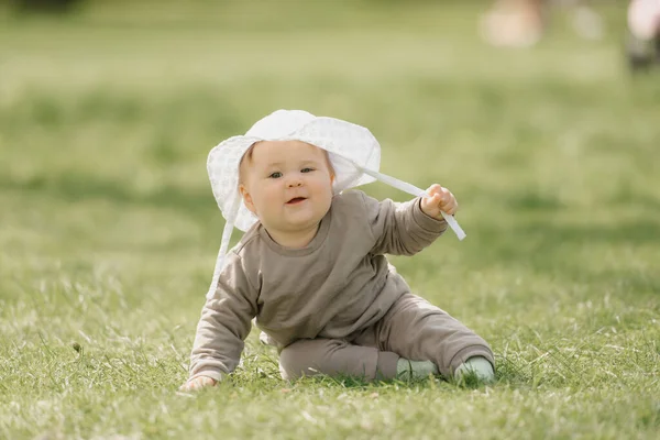 Beyaz panama şapkalı 7 aylık bir çocuk çayırda eğleniyor..