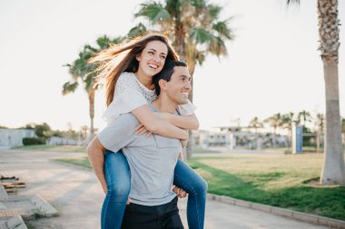 Mutlu bir esmer kız, İspanya 'da akşamları İspanyol erkek arkadaşına palmiyeler ve güneş ışınları arasında biniyor. Valencia 'da gün batımında bir çift turist..