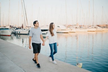 İspanya 'da akşam iskelede gezen esmer kız arkadaşıyla İspanyol bir adamın tam uzunluğunda bir fotoğraf. Birkaç turist Valencia 'da bir randevuda yatlara bakıyor..