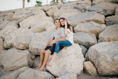 İspanyol bir adam, gülümseyen esmer kız arkadaşının bacaklarının arasında oturuyor. İspanya 'da bir dalgakıranın taşları üzerinde. Valencia 'da gün batımında bir çift turist..