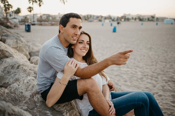 Bir kadın, İspanya 'da bir dalgakıranın taşlarının üzerinde İspanyol erkek arkadaşının bacaklarının arasında oturuyor. Bir adam gün batımında karısına sarılıyor. Adamın biri Valencia 'yı işaret ediyor..