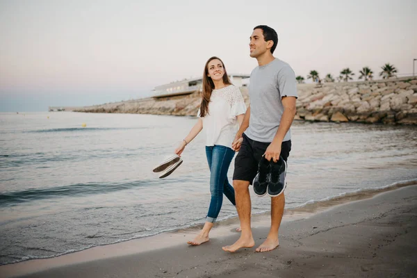 İspanya 'da, Balear Denizi' nin kıyısındaki kumlu bir plajda çıplak ayakla dolaşan, gülümseyen kız arkadaşıyla İspanyol bir adamın tam boy fotoğrafı. Valencia 'da randevusu olan iki turist.