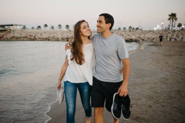 İspanyol bir adam ve gülümseyen kız arkadaşı akşamları İspanya 'da Balear Denizi' nin kıyısında kumlu bir plajda dolaşırken birbirlerine sarılıyorlar. Valencia 'da randevusu olan iki turist..
