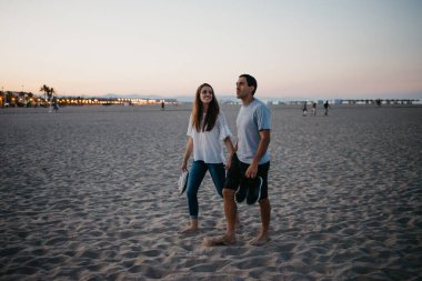 İspanyol bir adam ve gülümseyen kız arkadaşı akşam İspanya 'da Balearic Denizi yakınlarında kumlu bir plajda geziniyorlar. Valencia Alacakaranlık 'ta buluşan iki turistin tam boy fotoğrafı..