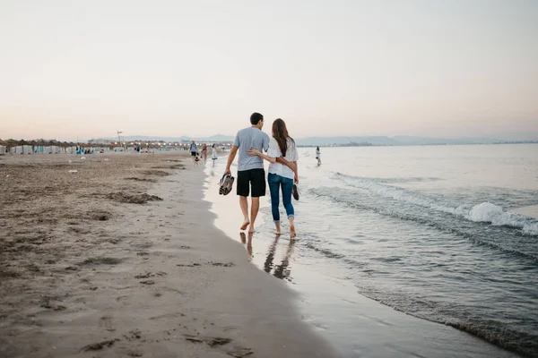 スペインの夕暮れ時に裸足でビーチで抱き合っている男と女の後ろからの写真 バレンシアのバレアレス海の近くの日付の観光客のカップル — ストック写真